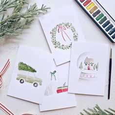 four christmas cards with watercolors and pencils on the table next to them