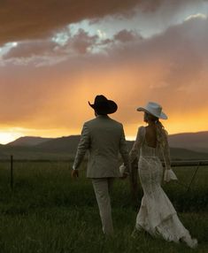 a bride and groom are walking through the grass at sunset with mountains in the background