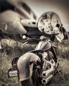 a motorcycle parked in front of an airplane on the grass with another plane behind it