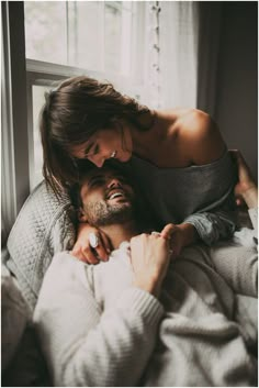 a man and woman cuddle together in front of a window