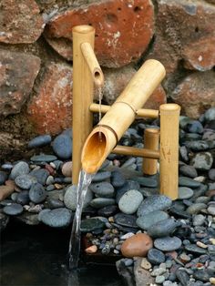 a water fountain made out of bamboo sticks is shown in front of a rock wall