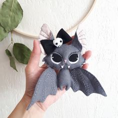 a hand holding a small gray cat with a skull on it's head and wings