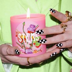 a woman holding a pink candle with black and white nail polishes on her nails