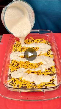 someone adding cheese to a casserole dish with sour cream being poured on top