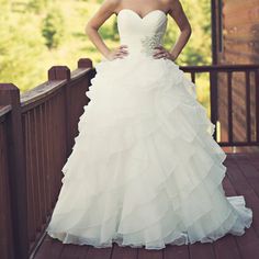 a woman in a white wedding dress standing on a wooden deck with her hands on her hips