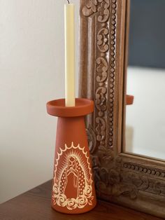 an orange candle holder with a lit candle in it sitting on a table next to a mirror