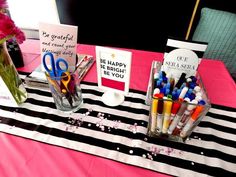 two vases filled with pens and markers on top of a pink table cloth covered table