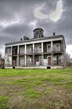 an old abandoned house sitting on top of a lush green field under a cloudy sky