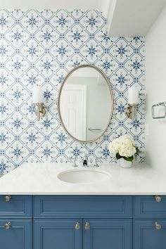 a bathroom with blue and white wallpaper and a round mirror on the wall above it