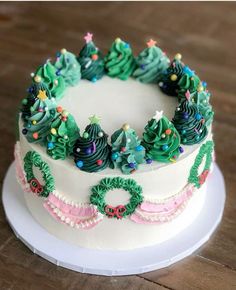 a decorated christmas cake sitting on top of a white plate with green frosting and trees