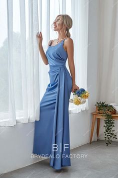 a woman standing in front of a window wearing a blue dress and holding a bouquet