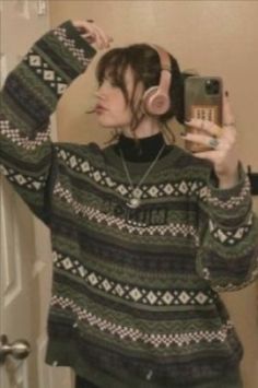 a woman taking a selfie in front of a mirror wearing headphones and sweater