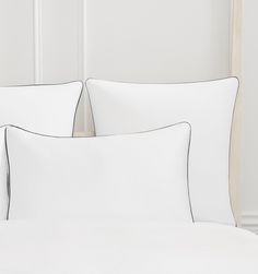 two white pillows sitting next to each other on top of a bed with white sheets