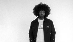 a man with an afro standing in front of a white wall