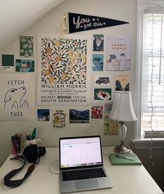 a laptop computer sitting on top of a white desk next to a lamp and window