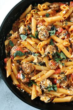 pasta with meatballs and spinach in a skillet on a white table top