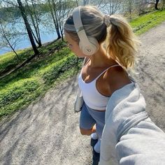 a woman with headphones on walking down a road next to the water and trees