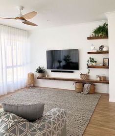 a flat screen tv sitting on top of a wooden shelf in a living room next to a window