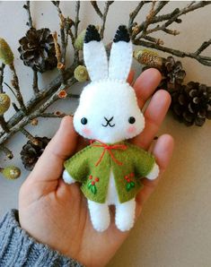 a hand holding a small stuffed animal in it's left hand next to some pine cones