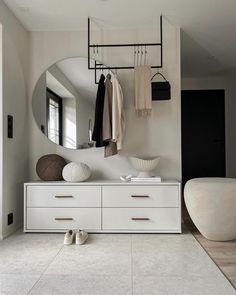 a white dresser sitting under a mirror next to a wall mounted coat rack with clothes hanging on it