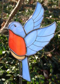 a stained glass bird sitting on top of a metal pole in front of some bushes