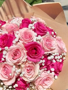 a bouquet of pink roses sitting on top of a brown paper bag filled with baby's breath