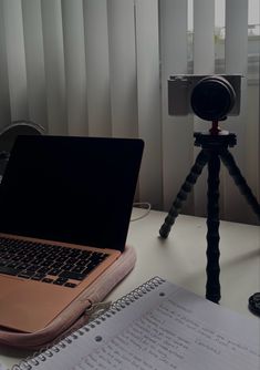 an open laptop computer sitting on top of a desk next to a camera and notebook