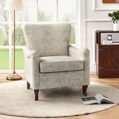 a living room with a chair, lamp and book on the floor in front of a window