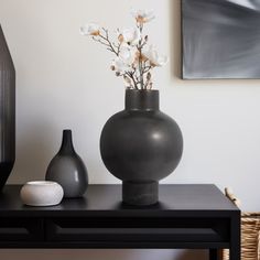 two vases with flowers in them on a black table next to a painting and wicker basket