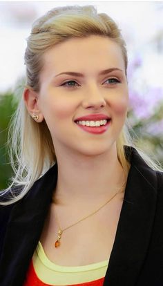 a woman with blonde hair smiling and wearing a black blazer over an orange top