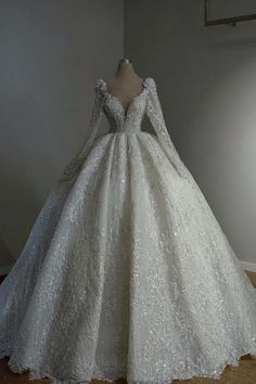 a white wedding dress with long sleeves and a train on display in front of a wall