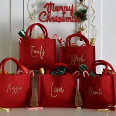 four red bags with merry christmas written on them sitting in front of a sign that says merry christmas