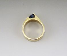 Presented is a stunning 14 karat gold and sapphire ring. This is a modern piece, likely of American make. The ring is channel set with a round faceted sapphire of about half a carat in size, maybe as much as 60 points. This is a real, mined-from-the-ground stone, with vibrant blue color. The gold setting is sleek and attractive, holding the stone in an interesting off-set design. The ring is in great condition. The stone is securely set. There are some slight abrasions to the surface of the ston Modern Yellow Gold Sapphire Ring With Center Stone, Modern Sapphire Ring For Anniversary, Modern Round Cut Sapphire Ring For Anniversary, Modern Sapphire Ring With Brilliant Cut For Anniversary, Modern Sapphire Ring With Tension Setting And Round Band, Modern Yellow Gold Sapphire Ring With Round Cut, Modern 14k Gold Sapphire Ring With Center Stone, Modern Solitaire Sapphire Ring, Modern Sapphire Birthstone Ring