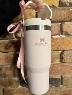 a person holding a white travel mug with pink ribbon around the neck and hand on brick wall