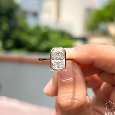 a woman's hand holding an engagement ring in front of her face with the diamond setting on it