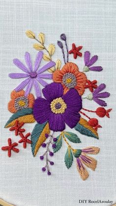 an embroidered flower is shown on a white piece of cloth with red, yellow and purple flowers