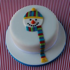 a white cake with a snowman decoration on the top and striped table cloth behind it