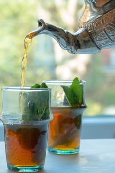 tea being poured into two cups with mint leaves in the cup and another glass on the table