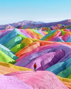 a person standing in the middle of a field covered with colorful hills and trees,