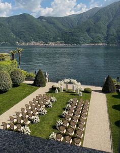 an outdoor ceremony set up with chairs and flowers on the lawn by the water in front of mountains