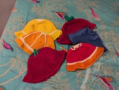 three knitted hats laying on top of a bed next to an orange, yellow and red hat