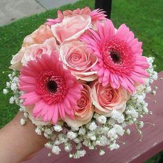 a bouquet of pink and white flowers sitting on top of a wooden bench next to grass