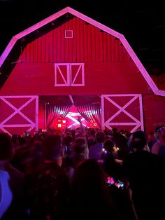 a large group of people standing in front of a red barn with lights on it