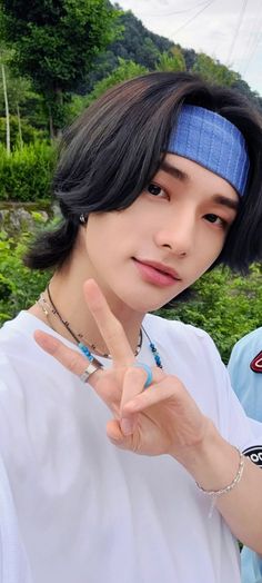 a young man making the peace sign with his hand while standing in front of some trees