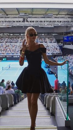 a woman in a short black dress is walking down the runway at a tennis match