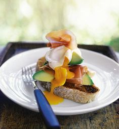 a white plate topped with an open face sandwich next to a blue fork and knife