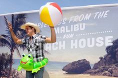 a man holding a beach ball and inflatable frog toy on his arm while standing next to a sign