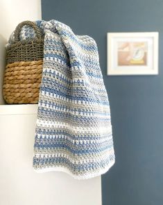 a blue and white crocheted blanket sitting on top of a shelf next to a basket