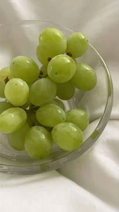 a glass bowl filled with green grapes on top of a white tablecloth covered surface