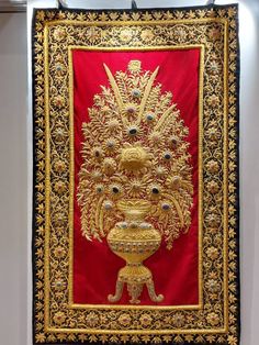 a red and gold wall hanging with an ornate design on it's side in a room